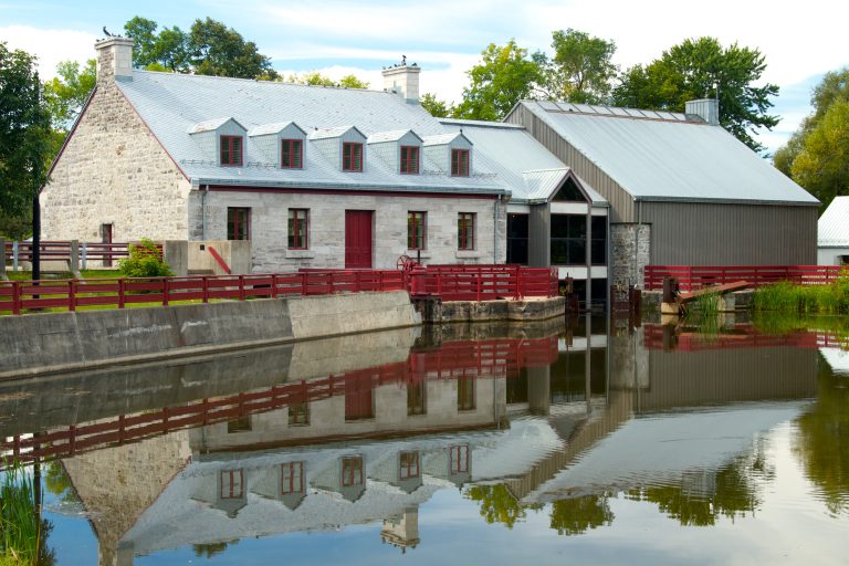 Moulin à eau historique en pierre avec clôture rouge et réflexion sur l'eau.