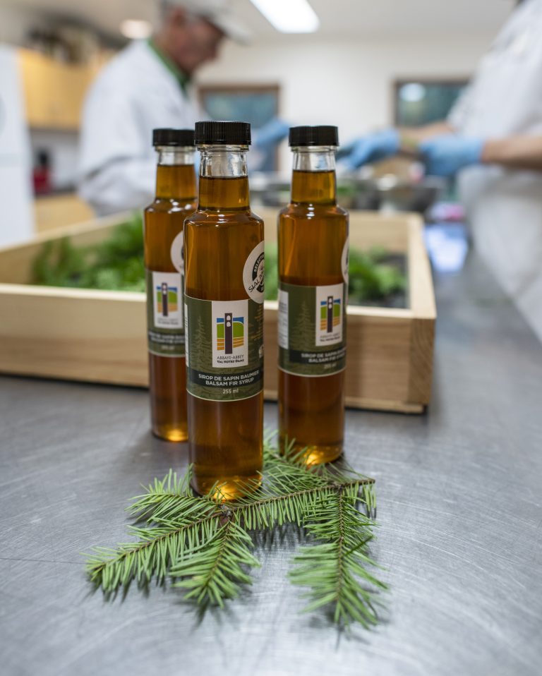 Trois bouteilles d'huile d'olive avec étiquettes, brins de romarin en avant, cuisine en arrière-plan.
