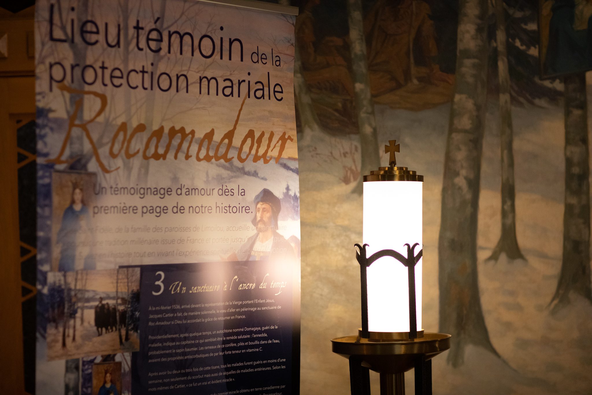 Murale de forêt et affiche du LIeu témoin de la protection Mariale Rocamadour. Une lanterne allumée se trouve à l'avant plan en format 768 x 512